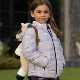 Young girl wearing a light purple puffer jacket with animal patterns, holding a plush toy, outdoors.
